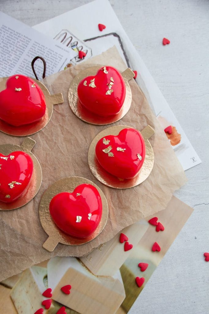 Delicious heart-shaped red mousse cakes with gold accents on parchment paper, perfect for Valentines Day.