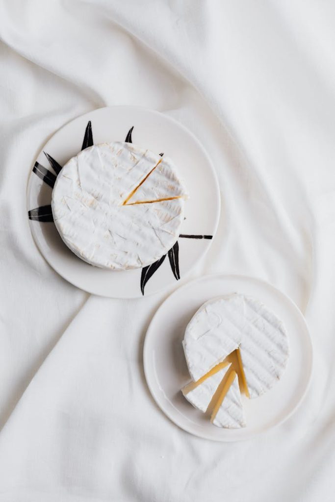 Stylish flatlay of gourmet cheese wedges on ceramic plates with white fabric backdrop.